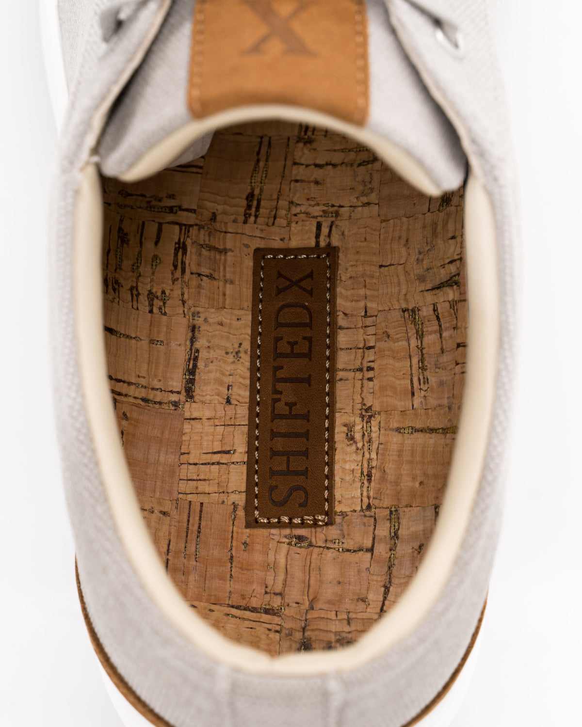 Close-up of a white sneaker with a brown insole and brand label on a white background